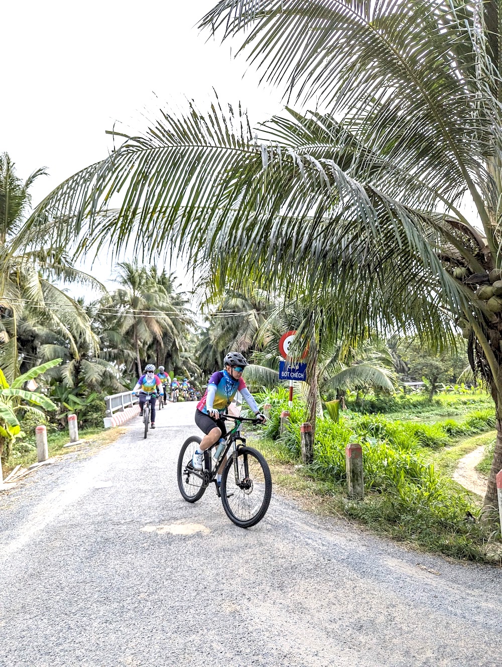 Cyclist riding through a rural village with stilt houses and palm trees in the Mekong Delta, Southern Vietnam.